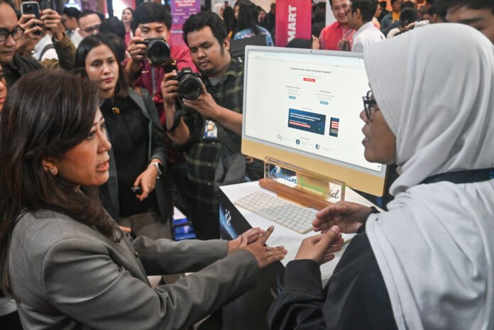 Menteri Komunikasi dan Digital (Menkomdigi) Meutya Hafid (kiri) berbincang dengan petugas di stan Kementerian Komdigi pada peluncuran Senyum Nyaman dengan Biometrik (SEMANTIK) di Gedung Sarinah, Jakarta, Selasa (27/1/2026).